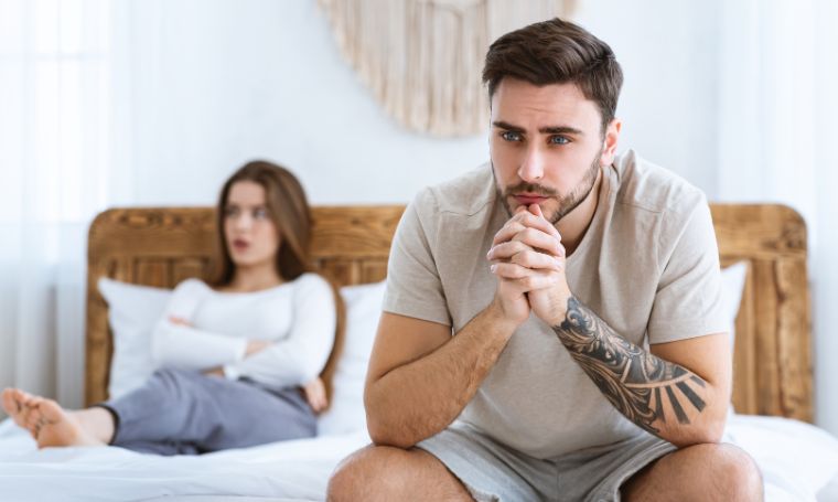 zmartwiony-mezczyzna-siedzi-na-lozku-partnerka-w-tle-problemy-z-libido